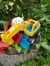 Ein bunter Spielzeigbagger in einem Garten. Die Schaufel des Spielzeugbaggers ist mit Wasser gefüllt.